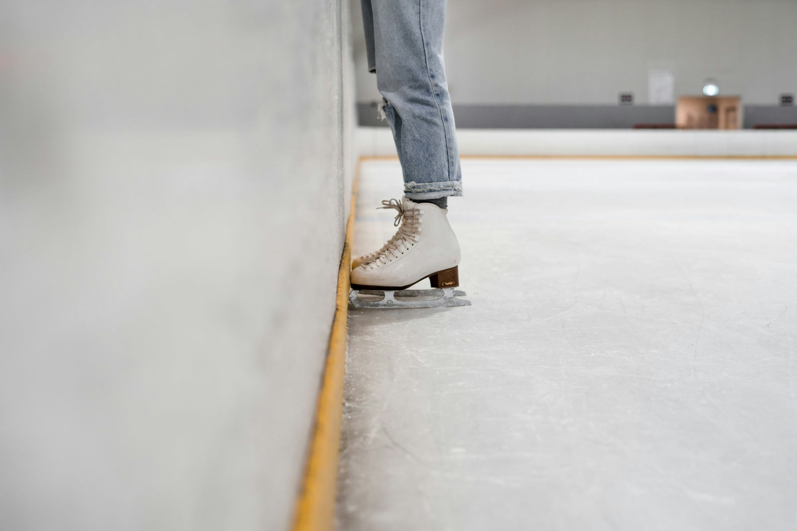 A person in ice skates standing still on an ice rink near the wall. 