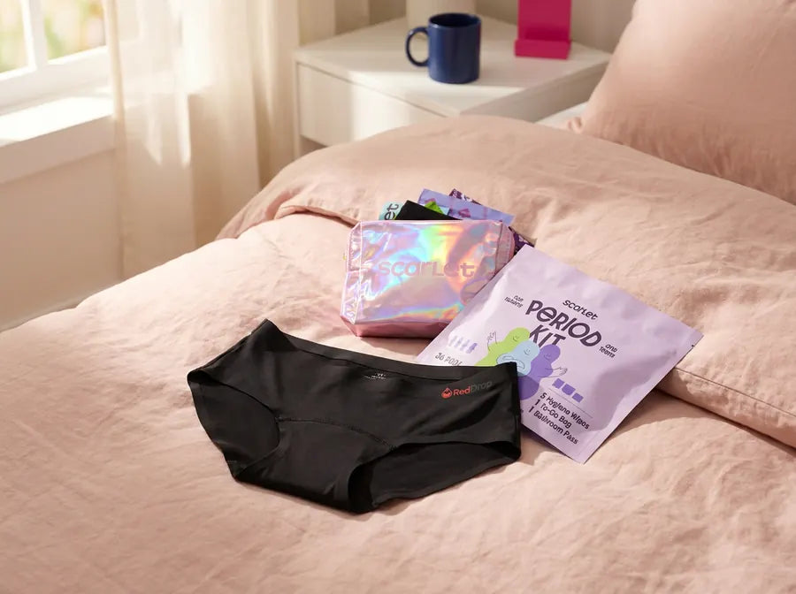 Scarlet period underwear on a bed with the pouch and Period Kit