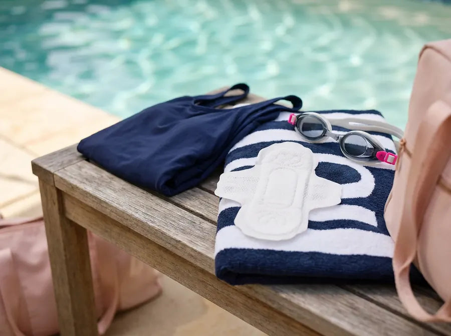A pad sitting on a pool bench next to a swimsuit and goggles